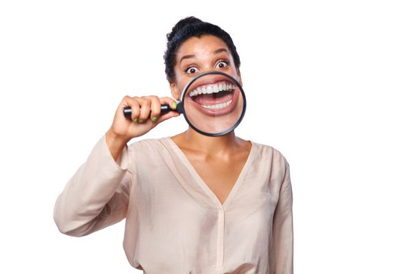 تصویر خنده دار از زن هیجان زده و خندان و نشان دادن دندان ها از طریق یک ذره بین بر روی زمینه سفید