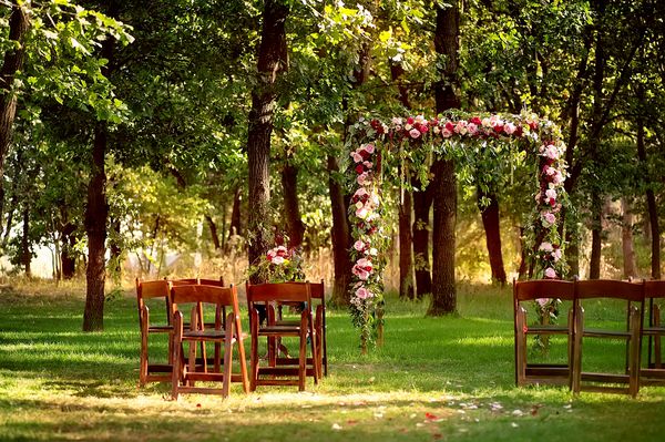 طاق عروسی که با گل و صندلی های چوبی در جنگل های عمیق تابستانی تزئین شده است تصویر با تمرکز نرم