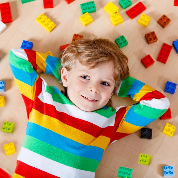 کودک کوچک با تعداد زیادی بلوک پلاستیکی رنگارنگ در محیط داخلی پسر بچه مبارک با پوشیدن پیراهن رنگارنگ و لذت بردن از ساخت و ایجاد