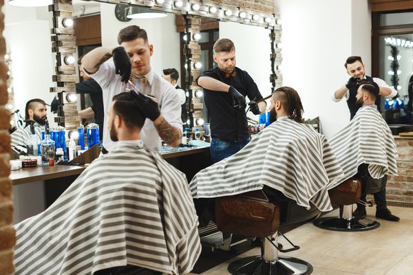 سه مرد شیک جوان با موهای تیره که در آرایشگاه نشسته اند و آرایش مو را انجام می دهند آینه های بزرگی در کنار مردان است