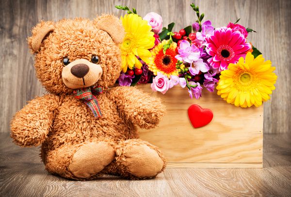 دسته گل و خرس عروسکی روی زمینه چوبی