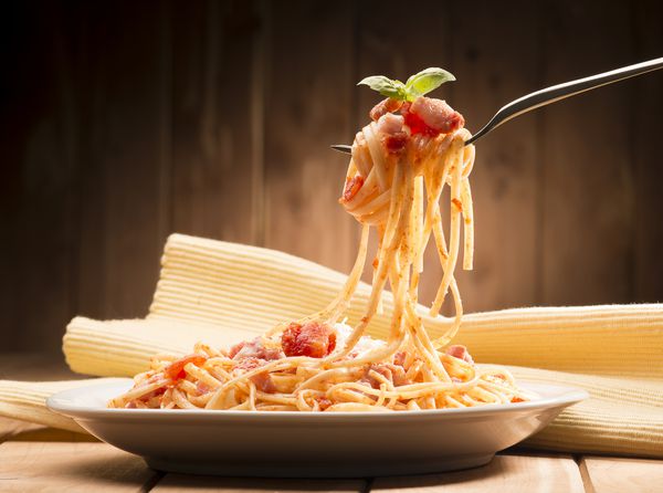 اسپاگتی با سس آماتریکانا در ظرف روی میز چوبی قرار دهید
