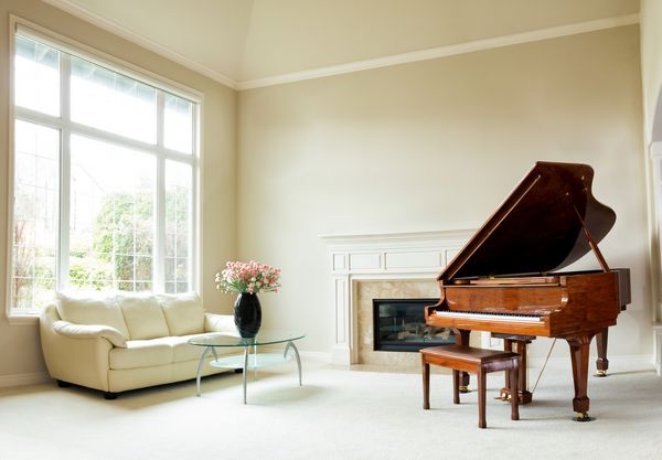 اتاق نشیمن با پیانوی بزرگ شومینه مبل و پنجره بزرگ با نور روز روشن که وارد اتاق می شود