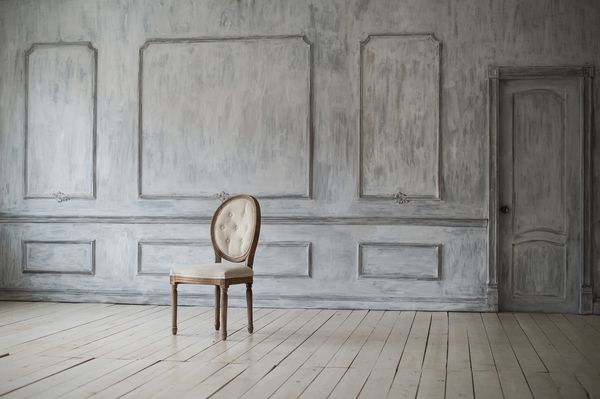 صندلی پرنعمت سفید در مقابل یک دیوار سبک با قالبهای کف پارکت چوبی ایستاده است