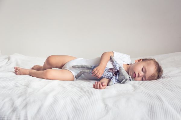 کودک خوابیده در گهواره خود یک خرس عروسکی را در دست دارد