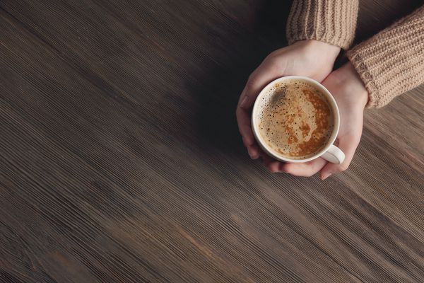 دستهای زن که فنجان قهوه را روی زمینه چوبی نگه می دارند