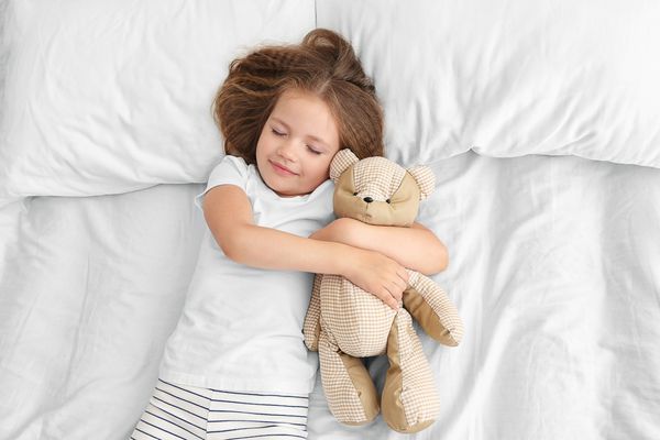 دختر کوچولوی ناز با خرس عروسکی در رختخواب