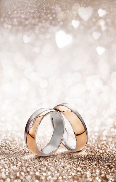 پس زمینه جشن حلقه عروسی رمانتیک با دو حلقه طلایی که به صورت عمودی بر روی یک پس زمینه درخشان با قلب های سفید تعادل می یابد و فضای کارت را برای دعوت یا کارت تبریک کپی می کنید