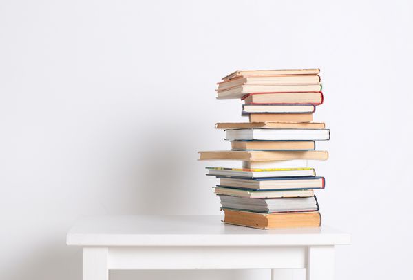پشته کتابهای شومیز روی میز سفید با زمینه دیواری سفید در طول مطالعه یا کار تعداد زیادی از منابع را در مورد تعداد زیادی از منابع مرتبط جستجو کنید