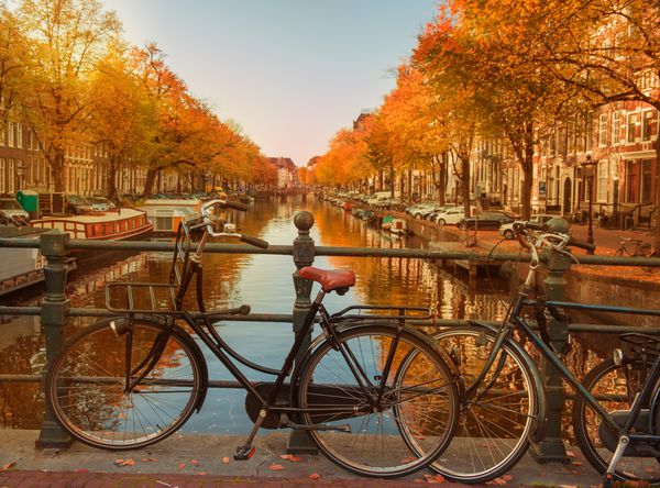 عصرها در کانالهای زیبای آمستردام در پاییز دوچرخه هایی که در پل های پیش زمینه پارک شده اند