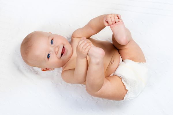 کودک کمی خنده دار که پوشک را روی یک پتو بافتنی سفید در یک مهد کودک آفتابی پوشیده است کودک بعد از حمام یا دوش گرفتن روی حوله تازه تغییر ناراحتی نوزادان و مراقبت از پوست بچه ناز با پاهایش