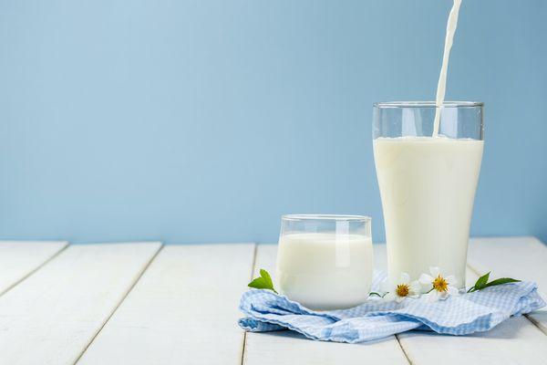 ریختن یک لیوان شیر روی یک میز چوبی سفید روی زمینه آبی مفهوم لبنیات مغذی و سالم