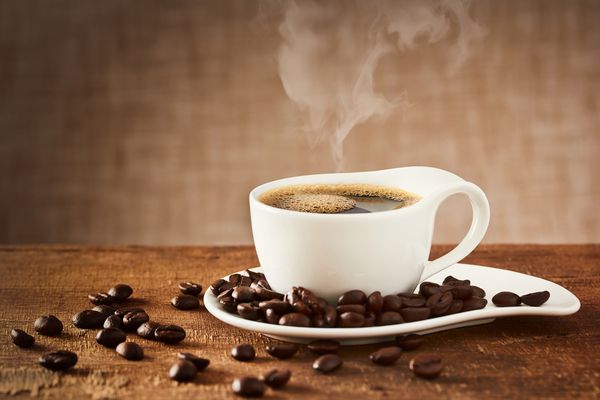 فنجان قهوه و نعلبکی روی یک میز چوبی با دانه های قهوه