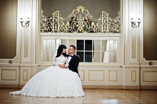 زن و شوهر عروسی باشکوهی که روی صندلی روی اتاق سلطنتی و آینه های زیادی نشسته اند