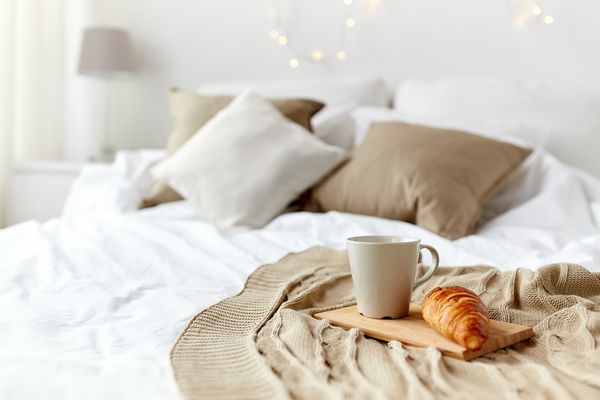 صبحانه دنج صبح تعطیلات و مفهوم زمستان اتاق خواب دنج با فنجان قهوه و کروسان در تخته چوبی در رختخواب در خانه