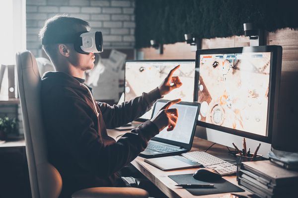 بازی های تست جوانی که هنگام نشستن در میز کار خود در دفتر خلاقانه از هدست واقعیت مجازی استفاده کرده و در حال حرکت است