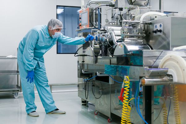 دانشمند قفقازی خم شده در لباس آزمایشگاه آبی سعی در تعمیر دستگاه تولید با شفت