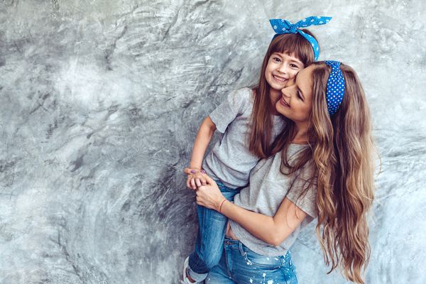 مادر جوان زیبا با دخترش تی شرت خاکی خاکستری و شلوار جین را در مقابل دیوار بتونی خشن سبک مد مینیمالیستی خیابان همان نگاه خانوادگی لباس برای والدین و کودک پوشیده است