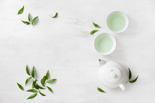 مفهوم چای دو فنجان چای سفید و قوری که با برگهای چای سبز احاطه شده اند از بالا منظره برای متن