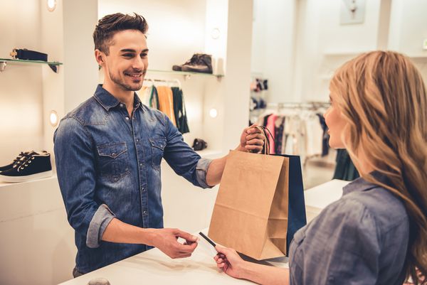 دستیار خوش تیپ فروشگاه هنگام خرید و کارت اعتباری به مشتری زیبا لبخند می زند
