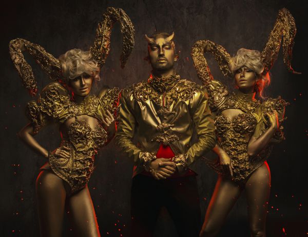 زنان شیطان زیبا با شاخ های زینتی طلایی و مرد شیطان خوش تیپ در ژاکت زینتی در زمینه تیره