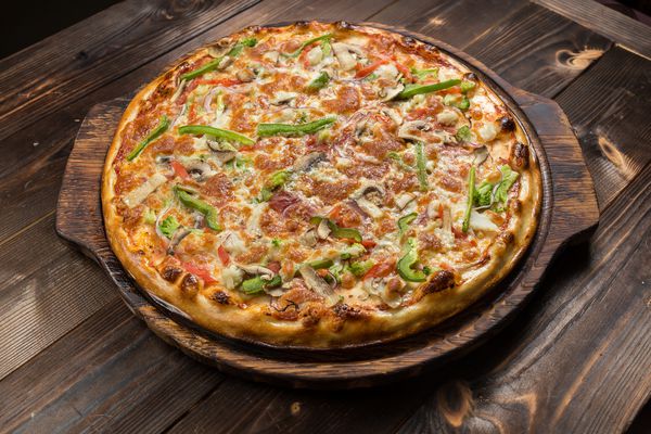 پیتزا خوشمزه با قارچ پوسته نازک شیرینی جدا شده در پس زمینه چوبی روی میز چوبی