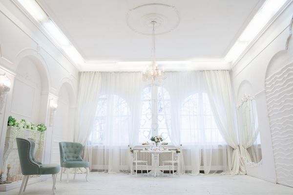 صندلی های پرنعمت نعناع در اتاق داخلی سفید کلاسیک با آینه خلاق پنجره بزرگ و گل های بهاری در گلدان های روی میز افقی