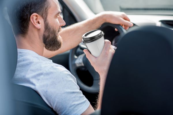 مرد خوش تیپ و لباس عروسکی با تی شرت سفید رانندگی یک ماشین با قهوه برای رفتن