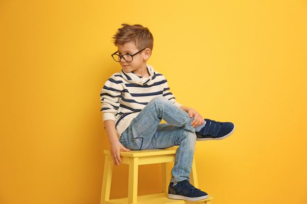 پسر زیبا و شیک ای که روی صندلی نزدیک دیوار رنگی نشسته است