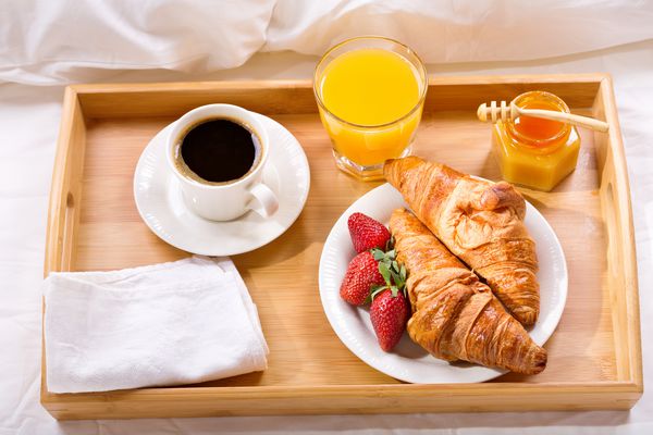 سینی صبحانه در رختخواب قهوه کروسان آب میوه و توت فرنگی تازه