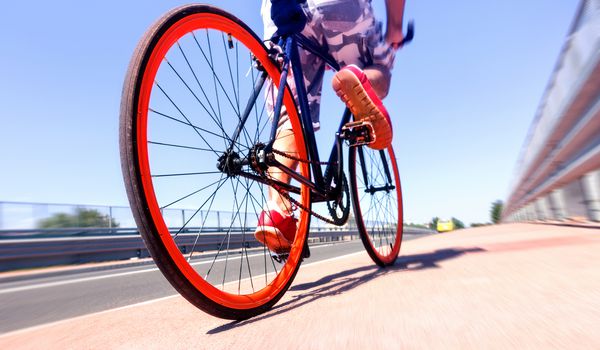 دوچرخه سواری مرد بر روی دوچرخه ورزشی چرخ های دوچرخه و چشم انداز جاده با دوچرخه سوار سوار پس زمینه آسمان آبی تابستانی مفهوم حمل و نقل جایگزین سازگار با محیط زیست با فیلتر زوم شعاعی
