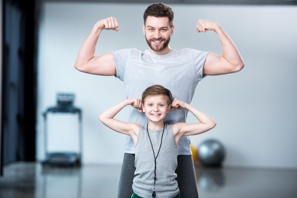 پسر با مرد جوان مربی یا پدرش که عضلات خود را نشان می دهد