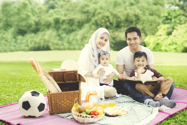 تصویری از خانواده شاد مسلمان که هنگام عکس گرفتن با یک کتاب در پارک به دوربین نگاه می کنند