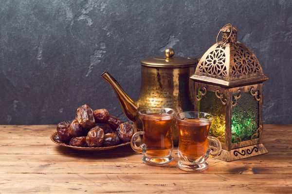 فانوس روشن فنجان های چای و خرما روی میز چوبی بر روی زمینه تخته سیاه مفهوم جشن تعطیلات رمضان کریم