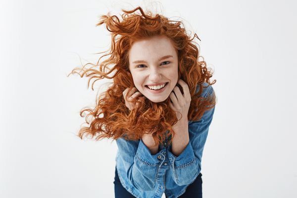 دختر سرخ بسیار و با موهای مجعد پرواز که می خندد با خنده به دوربین نگاه می کند تا از پس زمینه سفید استفاده کند