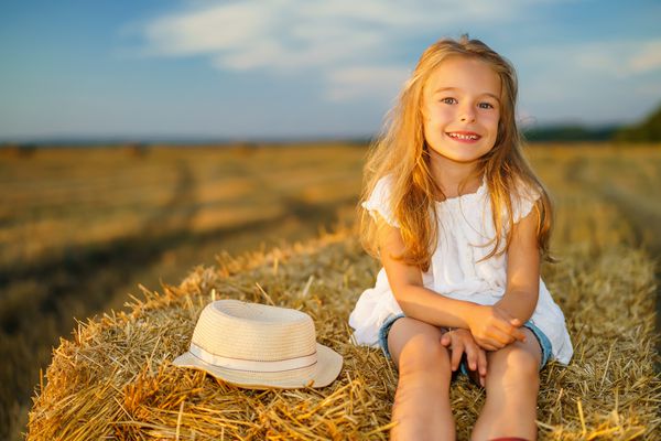دختر کوچک مبارک در یک زمینه با یونجه در غروب آفتاب