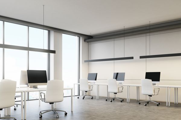 صفحه های رایانه خالی که روی یک میز در یک دفتر سفید با پنجره های بزرگ ایستاده اند مفهوم یک شرکت موفق رندر سه بعدی را مسخره کنید