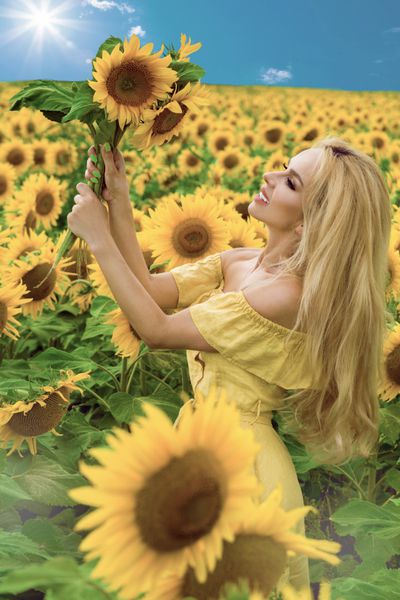 زن زیبایی که روی یک علفزار با گلهای آفتابگردان ایستاده و با خوشحالی لبخند می زند