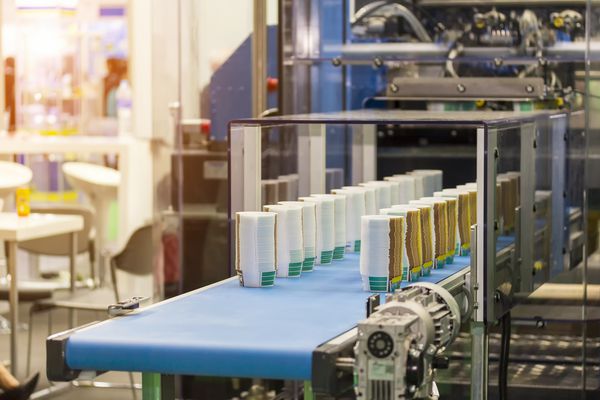 ردیف بسیاری از لیوان های کاغذی روی تسمه نقاله اتوماتیک در طی فرآیند تولید در کارخانه