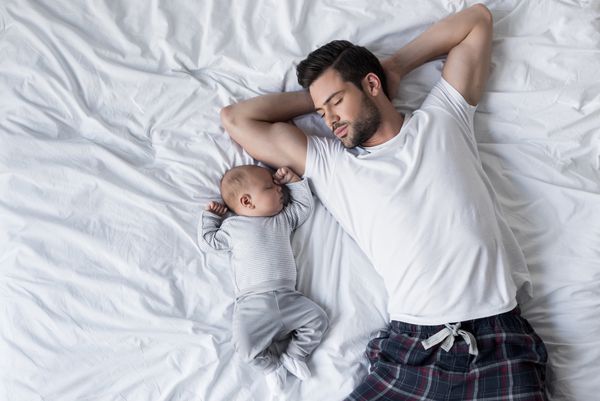 نمای برتر پدر خوش تیپ که در رختخواب با کودک کوچک خوابیده است