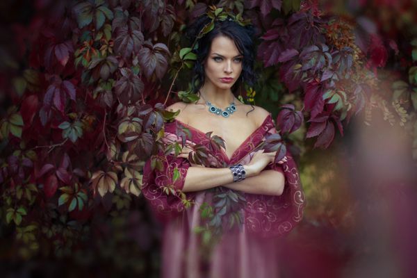 پرتره یک مدل زیبا در لباس مجلسی مد که با برگهای قرمز پاییزی احاطه شده است