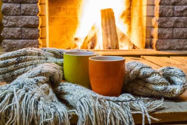 دو لیوان چای یا قهوه چیزهای پشمی در نزدیکی شومینه دنج در خانه کشور تعطیلات زمستانی افقی