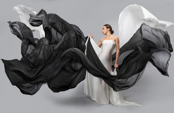 پرتره مد زن زیبا با لباس سفید و سیاه پارچه در باد پرواز می کند شبح های زنانه که از طریق آن قابل مشاهده هستند
