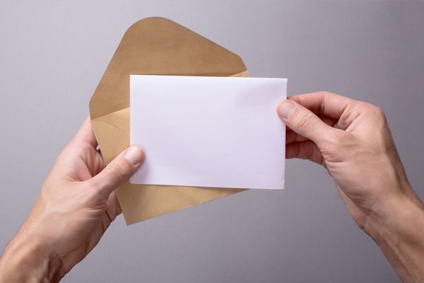 مرد یک نامه یا کارت پستال مسخره در دستان خود با پاکت روی یک پس زمینه خاکستری نگه می دارد