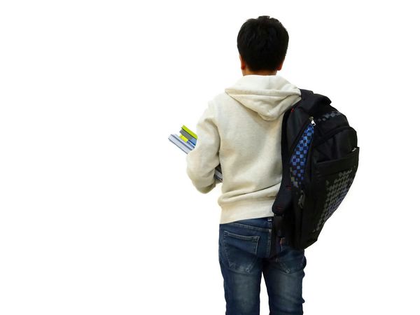 دانش آموز پسر در پارچه سفید و شلوار جین ایستاده است و کتاب های زیادی را روی دست دارد و کیف سیاه را روی شانه حمل می کند تا به دانشگاه برود