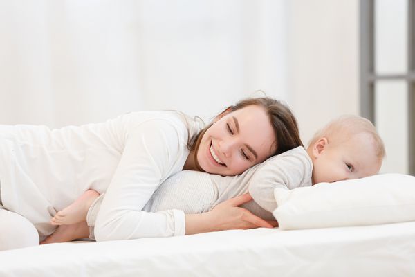 مادر جوان شاد و با پسر بچه کوچک خود که در خانه در رختخواب است خوابیده است پرتره خانوادگی لباس سفید فضای داخلی خانه