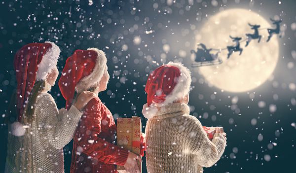 کریسمس مبارک و تعطیلات مبارک بچه های کوچک ناز با هدایای کریسمس بابانوئل در سورتمه خود در برابر آسمان ماه پرواز می کند کودکان و نوجوانان از تعطیلات با هدیه در زمینه تاریک لذت می برند