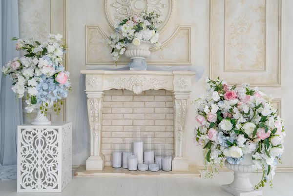 شومینه تزئینی با گل و شمع در نزدیکی دیوار آجری در اتاق فضای آزاد تزئین گل از گل های سفید و فضای سبز در گلدان های روی شومینه سفید