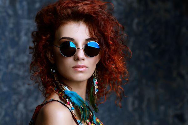 پرتره نزدیک از یک زن زیبا و روشن با موهای روباه فرفری در عینک آفتابی گوشواره و مهره سبک قومی در لوازم جانبی