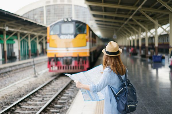 مسافر زن جوان با کوله پشتی و کلاه آبی به دنبال نقشه با سابقه قطار در ایستگاه قطار بانکوک سفر در بانکوک تایلند مفهوم سفر